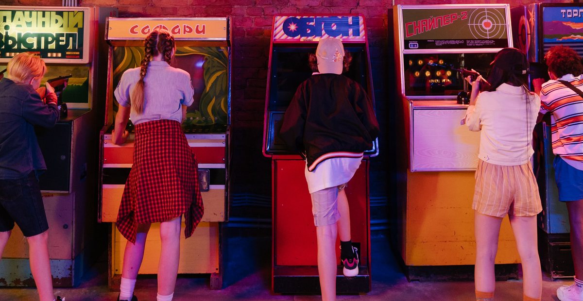 A group of friends playing arcade games together under neon lights