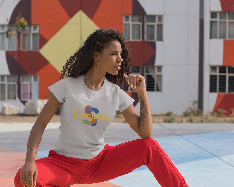 A woman stretching outdoors in a colourful urban court, wearing a Socially tee